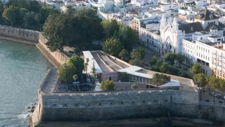 Vista aérea del Baluarte de la Candelaria, en Cádiz, con el paseo superior sobre la muralla, la Bahía de Cádiz a la izquierda y los edificios del casco histórico al fondo.