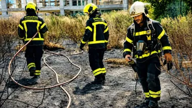 Zona de pastos quemada y varios bomberos sofocando el fuego.