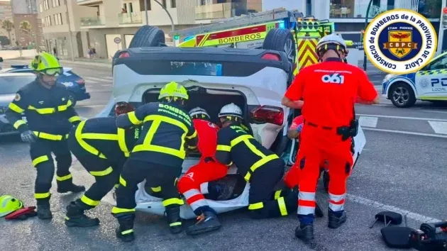 Bomberos tratando de sacar a la conductora del vehículo que está boca abajo.