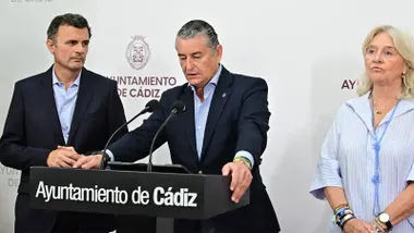 Antonio Sanz habla desde un atril con el logotipo del Ayuntamiento de Cádiz durante una comparecencia institucional. A su izquierda permanece el alcalde, Bruno García, mientras ambos aparecen ante un fondo con el escudo y el nombre del Ayuntamiento.