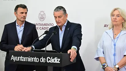 Antonio Sanz habla desde un atril con el logotipo del Ayuntamiento de Cádiz durante una comparecencia institucional. A su izquierda permanece el alcalde, Bruno García, mientras ambos aparecen ante un fondo con el escudo y el nombre del Ayuntamiento.