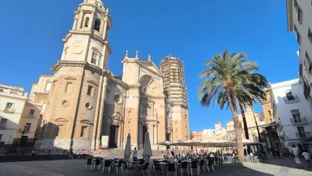 La Catedral de Cádiz en una mañana azul, con la Torre de Poniente con andamios y el tiovivo bajo ella