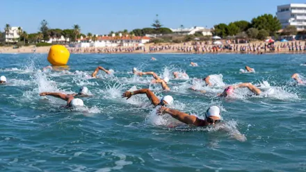 Muchas personas nadando en una playa, dentro de una competición.