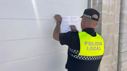 Momento en el que un policía local de Chiclana coloca la orden de derribo en una puerta de garaje de una casa.