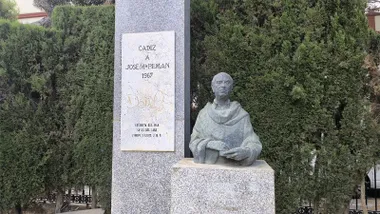 Monumento dedicado a José María Pemán en el Parque Genovés de Cádiz, con un busto de bronce sobre un pedestal de piedra junto a una placa conmemorativa, rodeado de árboles.