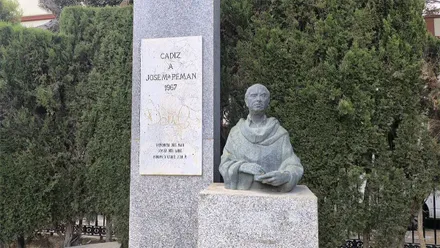 Monumento dedicado a José María Pemán en el Parque Genovés de Cádiz, con un busto de bronce sobre un pedestal de piedra junto a una placa conmemorativa, rodeado de árboles.
