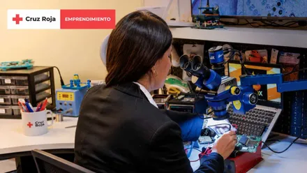Mujer reparando un aparato electrónico con lentes de aumento.