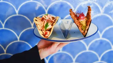 Mano de un camarero que lleva un plato con una sabrosa tapa.