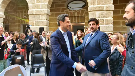 Jorge Vázquez saluda al presidente andaluz, Juanma Moreno, durante un acto institucional con público asistente.