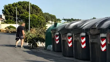 Una serie de contenedores alineados y una persona tirando ramas en un carrillo de mano.