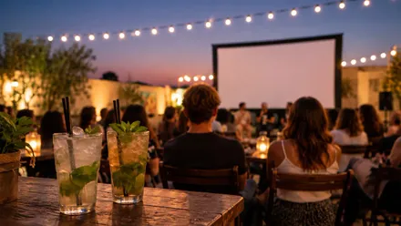 Personas entorno a una pantalla de cine y un vaso de mojito en una barra de bar.