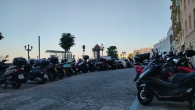 Vista del Campo del Sur de Cádiz con varias motos aparcadas junto al paseo y la Catedral al fondo, bajo un cielo azul completamente despejado que refleja el tiempo estable y soleado.