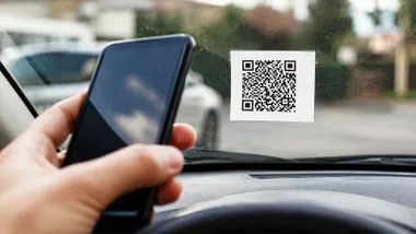 Mano con un móvil escanea un QR dejado en un parabrisas de un coche.