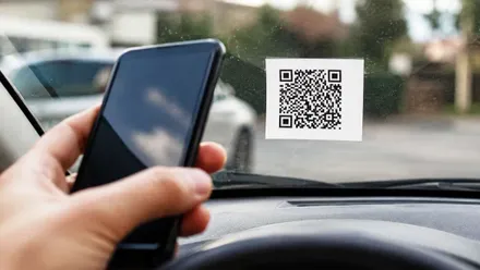 Mano con un móvil escanea un QR dejado en un parabrisas de un coche.