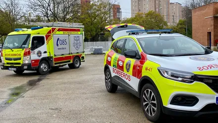 Un vehículo de mando SUV y un camión autobomba del Consorcio de Bomberos de la Provincia de Cádiz permanecen estacionados en un parque de bomberos. Ambos lucen los colores de alta visibilidad amarillo y rojo y están preparados para desplazarse al incendio forestal de Burgohondo, en Ávila. Al fondo se observan árboles, edificios y una zona urbana.