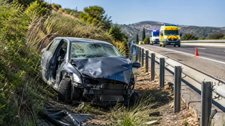 Coche accidentado a un lado de la carretera y ambulancia al fondo.