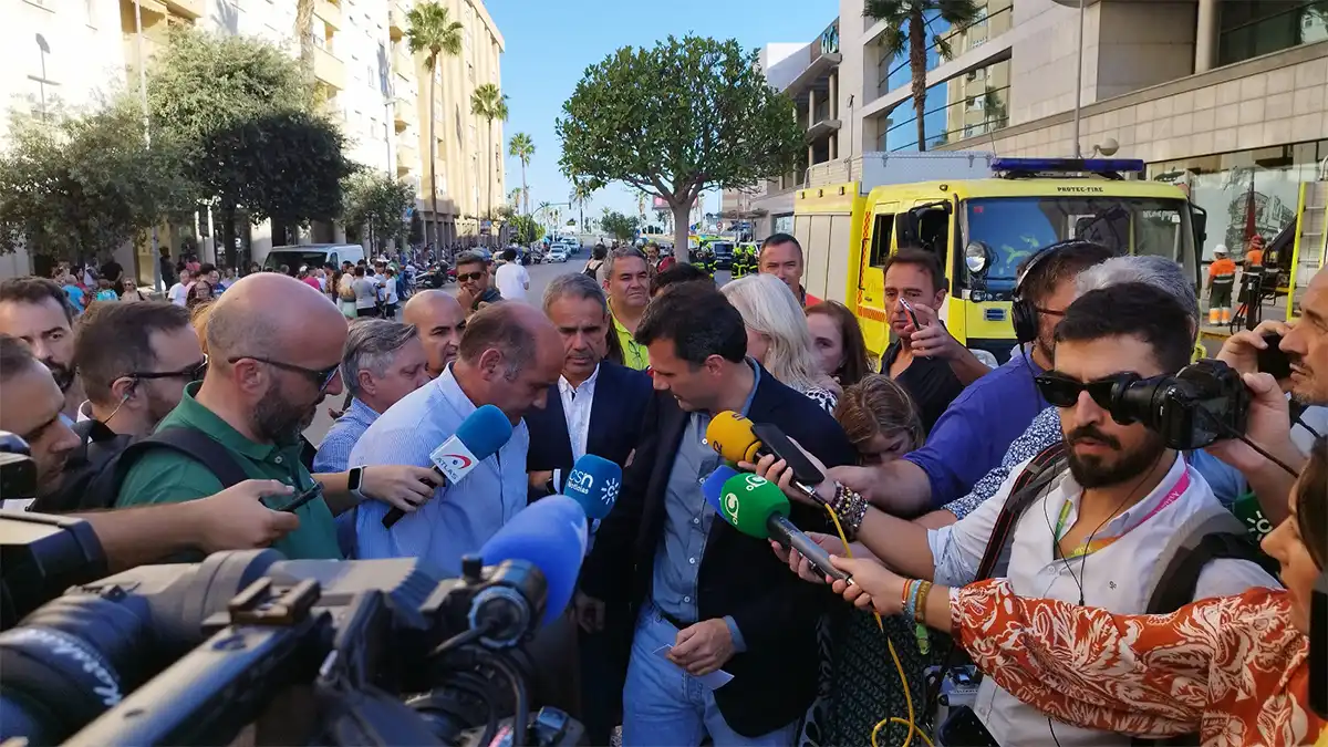 El alcalde de Cádiz, Bruno García, atiende a numerosos periodistas y cámaras en la calle, con un vehículo de emergencias al fondo.