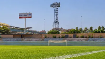 Césped con la vista de la portería y torre de luz del estadio Bahía Sur.