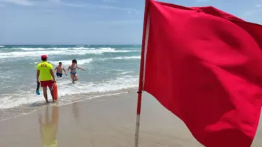 Socorrista indica a dos niños que deben salir del agua ante la bandera roja de prohibición de baño.