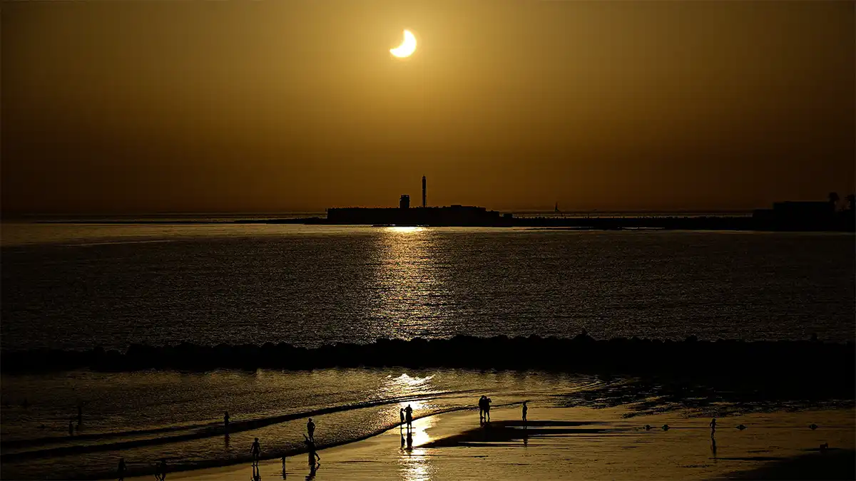 El Sol parcialmente eclipsado sobre el Castillo de San Sebastián y la playa de Santa María del Mar de Cádiz.