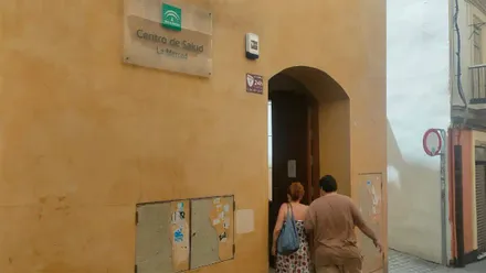 Fachada del Centro de Salud La Merced de Cádiz. Dos personas entran por la puerta principal del edificio, sobre la que se encuentra el cartel identificativo del centro sanitario.