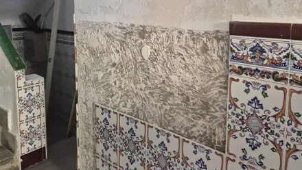 Pared interior de la finca de Lacave 9 con amplias zonas de pintura y revestimiento desprendidos y deteriorados por la humedad, junto a un zócalo de azulejos decorados.