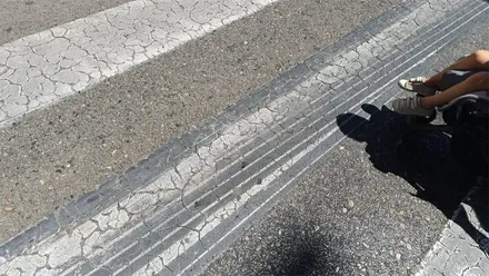 Varias marcas oscuras y alargadas de neumáticos atraviesan la calzada junto a un paso de peatones en la entrada a Cádiz.