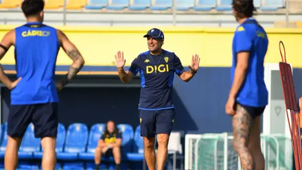 Imanol Idiakez, entrenador del Cádiz CF, gesticula con ambas manos mientras dirige un entrenamiento sobre el césped de la Ciudad Deportiva. Dos jugadores aparecen en primer plano y el técnico ocupa el centro de la imagen dando indicaciones al grupo.