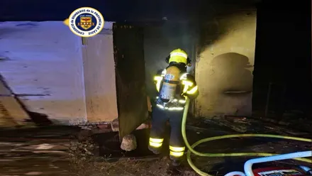 Cobertizo incendiado y un bombero entrando en el mismo.