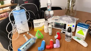 Imagen de una mesa con diverso material sanitario empleado en el cuidado de una menor con una enfermedad rara, entre el que se observan inhaladores, un nebulizador, suero, tubos de perfusión, medicamentos, un monitor médico y otros dispositivos para el tratamiento respiratorio.
