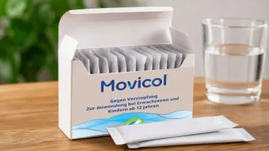 Cada de sobres de Movicol junto a un vaso de agua.