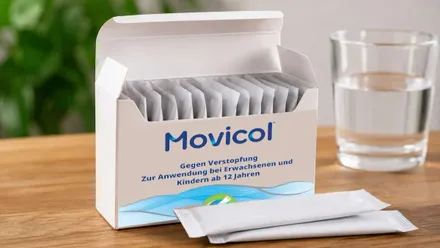 Cada de sobres de Movicol junto a un vaso de agua.
