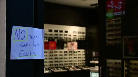Cartel escrito a mano en el escaparate de una óptica con el mensaje «No tenemos gafas para el eclipse», junto a expositores de gafas.