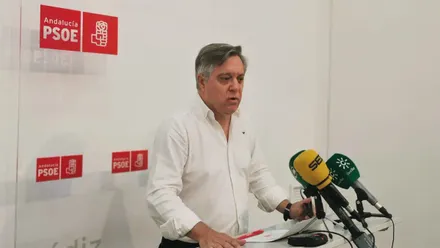 Óscar Torres comparece ante varios micrófonos en la sede del PSOE de Cádiz, con los logotipos del partido al fondo.