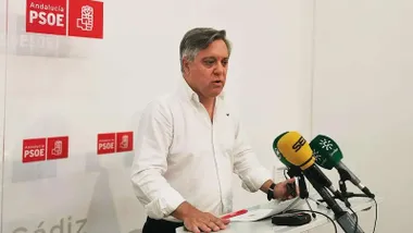 Con camisa blanca habla Óscar Torres, tras él un panel con el logotipo del PSOE.