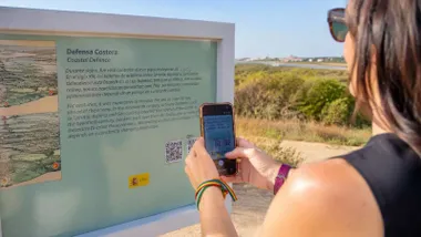 Chica con su móvil cogiendo el QR de un panel explicativo en Punta del Boquerón.