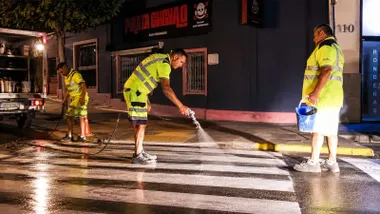 Tres operarios pintando un paso de cebra en la noche con iluminación.