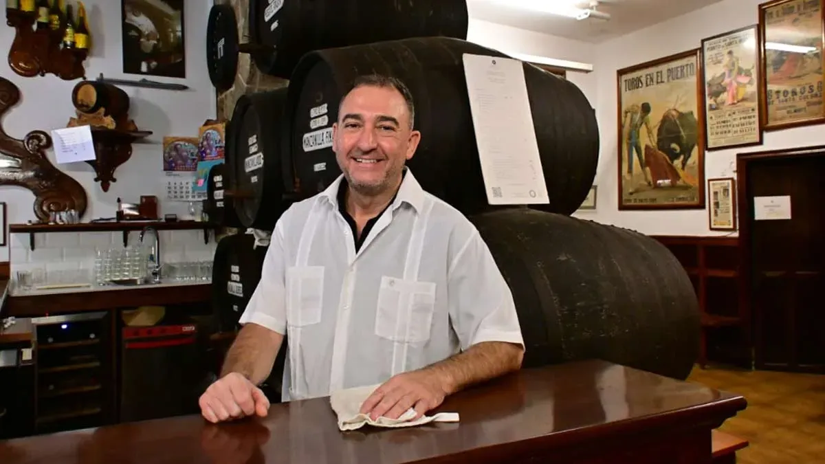 Camarero en la barra de madera, tras el los típicos barriles en color negro.