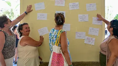 Cuatro mujeres observan y señalan numerosos folios con mensajes sobre vivienda pegados en una pared de la entrada del Ayuntamiento de Cádiz durante la protesta.