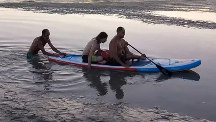 Dos personas sobre una tabla y otra empujándola en el agua.