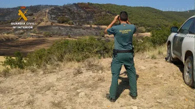 Junto a un coche patrulla un agente del Seprona mirando al monte con sus prismásticos.