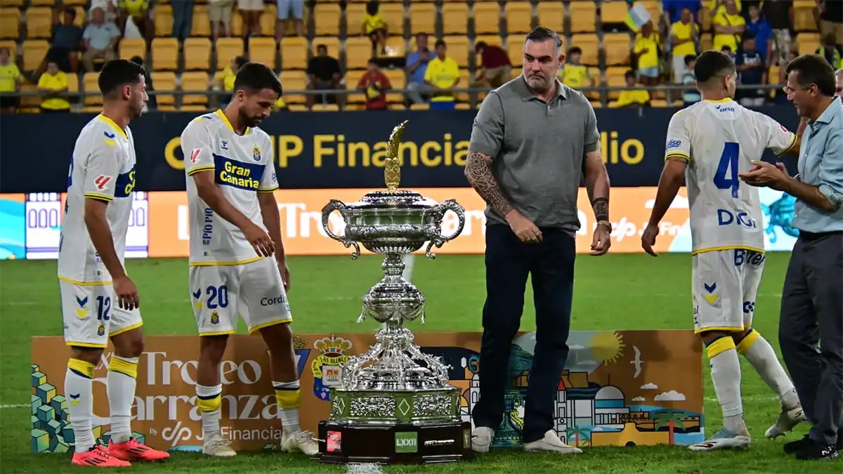 Christian Septien permanece junto al gran Trofeo Carranza sobre el césped mientras varios jugadores de Las Palmas se colocan a su alrededor y el alcalde de Cádiz, Bruno García, se acerca por la derecha.