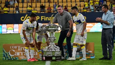 Christian Septien sujeta el gran Trofeo Carranza junto a varios jugadores de Las Palmas sobre el césped, mientras el alcalde de Cádiz, Bruno García, aparece a la derecha aplaudiendo.