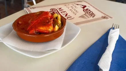 Una tapa servida en una cazuela de barro, hay una carta y un servicio de cubiertos.