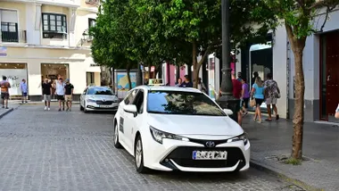 Dos taxis blancos estacionados en la parada de la plaza del Palillero de Cádiz, con peatones y comercios al fondo.