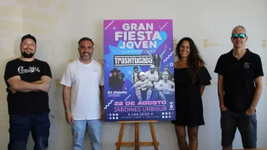 Junto al cartel del evento musical, en tonos azules y rosados está el delegado municipal de Juventud, Fede Díaz, acompañado por integrantes de Trashtucada.