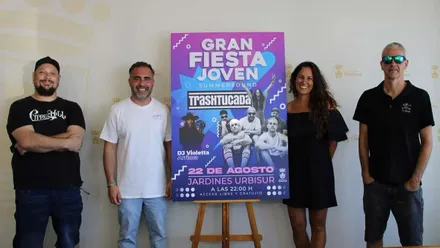 Junto al cartel del evento musical, en tonos azules y rosados está el delegado municipal de Juventud, Fede Díaz, acompañado por integrantes de Trashtucada.