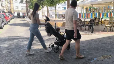 Una pareja camina con un coche de bebé por la plaza Manolo Santander de Cádiz, con una zona de juegos infantiles y terrazas al fondo.