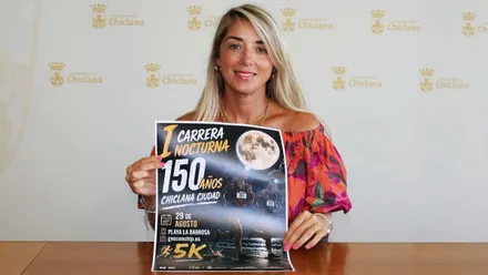 La delegada del Ayuntamiento de Chiclana, Isabel Butrón, muestra el cartel de la Carrera Nocturna de La Barrosa, con una luna y tonos oscuros.