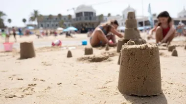 Primer plano de un castillo de arena y niñas y niños haciendo construcciones.